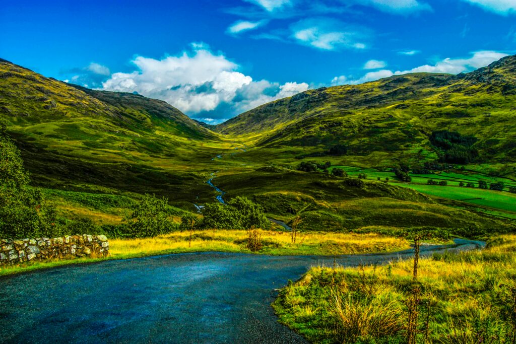 Vibrant countryside landscape featuring rolling green hills, a curving road, and a reflective stream.