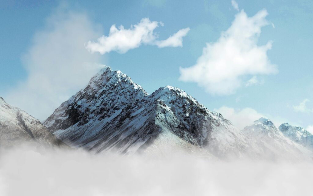 Rugged snow‑capped mountains breaking through low cloud, set against a vivid blue sky.