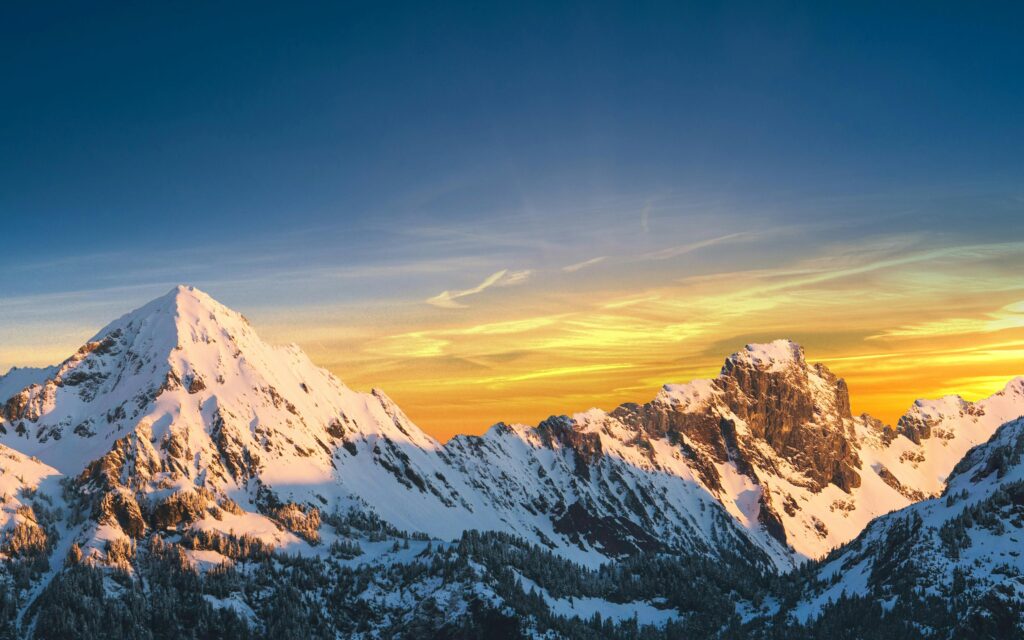 Dramatic alpine landscape with snow‑covered peaks illuminated by warm dawn light.